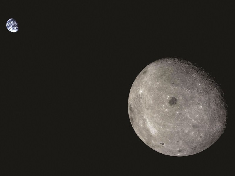 Image of the moon's far side with the Earth visible in the background against the blackness of space, captured by the 2014 Chang’e-5 T1 mission. The lunar surface appears gray and cratered, highlighting the rugged terrain of the moon.
