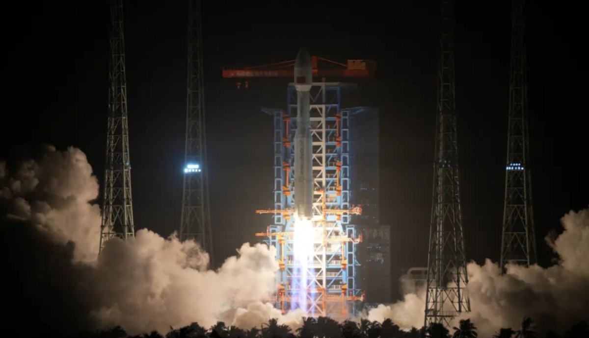 A Long March 8A rocket lifts off at night from the Hainan Commercial Space Launch Center, with bright flames and exhaust clouds illuminating the launch tower and surrounding gantry structures.