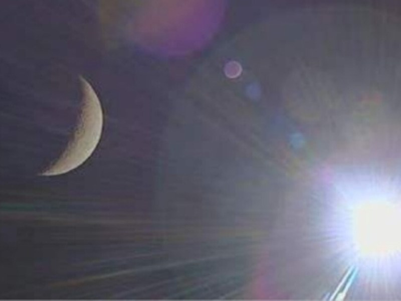 Image captured by Pakistan's iCube-Q CubeSat aboard China's Chang'e-6 mission, showing a crescent moon on the left and the Sun shining brightly on the right, with lens flares and scattered light effects.