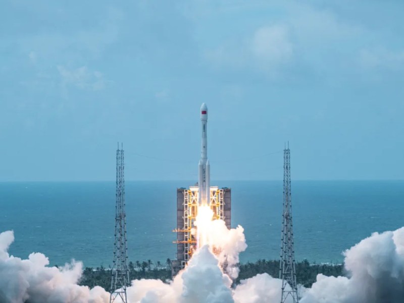 A Long March 7A rocket lifts off from Wenchang Satellite Launch Center on Hainan Island, leaving a trail of smoke and flames against the backdrop of the South China Sea.